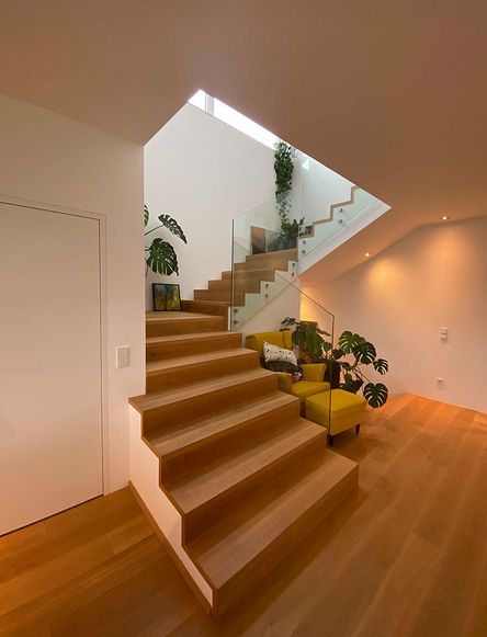Bild einer Holztreppe mit Glasgeländer und mit einem gelben Ohrensessel und gelben Hocker und einigen Pflanzen, modernes Hausdesign